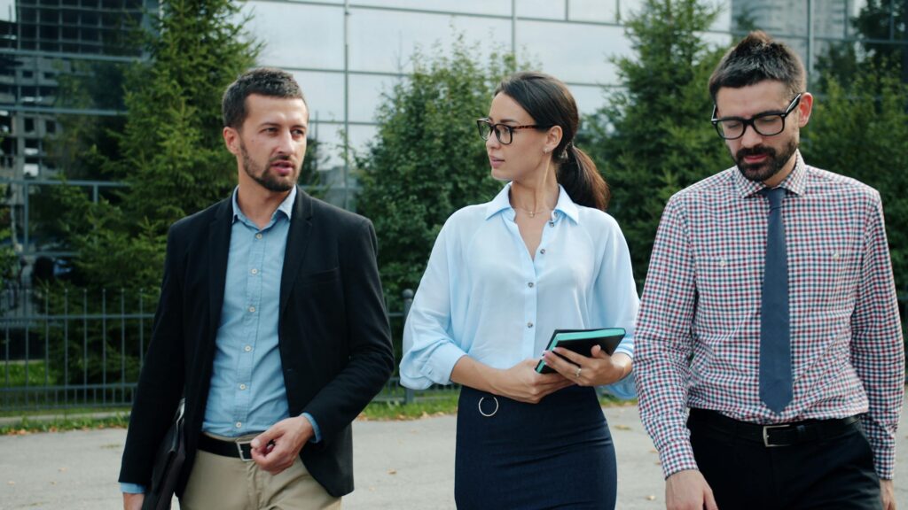 Three business professionals walking and discussing ideas outdoors in a modern urban setting.